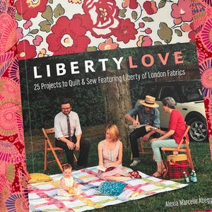 Puede incluir: Un libro titulado "LIBERTY LOVE" con el subtítulo "25 Projects to Quilt & Sew Featuring Liberty of London Fabrics". La portada presenta un diseño floral y una foto de personas en una manta de picnic. El libro está sobre una tela estampada.