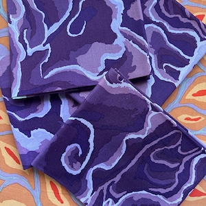 May include: Three square fabric napkins featuring a layered, abstract pattern in shades of deep purple, violet, and light lavender. The design consists of organic, flowing shapes that mimic geological strata or marbleised textures across the surface.
