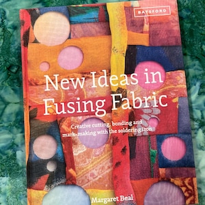 May include: A book titled "New Ideas in Fusing Fabric" by Margaret Beal. The cover features a colorful patchwork design with circular cutouts. The book's title and author's name are in white text.