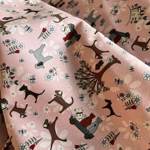 May include: A light pink fabric featuring a repeating pattern of various dog breeds, small trees, and flowers. Some dogs are depicted pulling small wagons containing cats. The design includes small butterflies and red tulips scattered throughout.