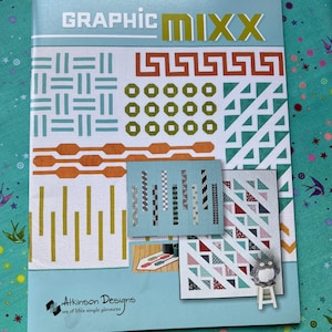 May include: A book titled "GRAPHIC MIXX" with geometric patterns in orange, green, and white. The cover also features the text "Atkinson Designs" and a small owl figurine on a miniature stool.