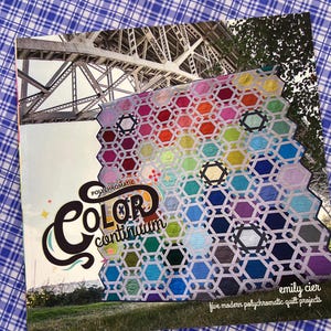 Könnte beinhalten: Ein Buchcover mit einem farbenfrohen Quilt mit einem geometrischen Muster. Der Quilt besteht aus sechseckigen Formen in einem Regenbogen von Farben. Der Titel "Color Continuum" wird mit dem Namen des Autors, "Emily Cier", und dem Untertitel "fünf moderne polychromatische Quiltprojekte" angezeigt.