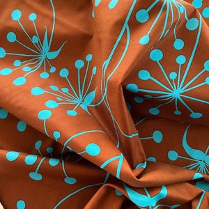 Könnte beinhalten: Brauner Stoff mit einem sich wiederholenden Muster aus türkisfarbenen floralen Designs. Der Stoff ist gefaltet und zeigt seine Textur und Tiefe. Die türkisfarbenen Elemente sind stilisierte Blumen und Samenkapseln.