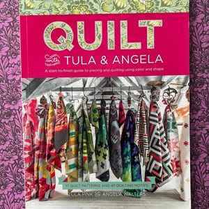 May include: A book titled "QUILT with TULA & ANGELA" with a pink cover and green floral accents. The book features a start-to-finish guide to piecing and quilting. The image also shows various colourful fabric swatches and the text "17 QUILT PATTERNS AND 47 QUILTING MOTIFS".