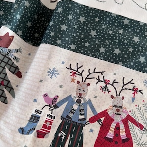 Può includere: Un tessuto con un motivo festivo di renne che indossano sciarpe e cappotti, che tengono calze con le scritte "His" e "Hers". Il design include bande verde scuro con motivi a stella, fiocchi di neve e altre illustrazioni a tema invernale.