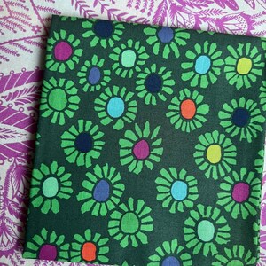 May include: A square piece of fabric featuring a dark green background with a repeating pattern of stylized flowers. The flowers have bright green petals and centers in various colors including purple, blue, light blue, yellow, and orange.