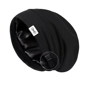 May include: Black beanie hat with a satin lining. The outer material is plain black, contrasting with the shiny, silky interior. A small white tag with a logo is attached. It has an adjustable strap.