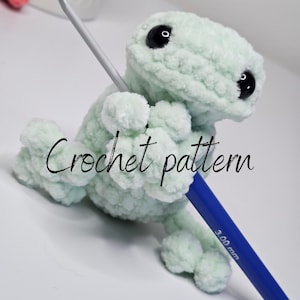 May include: A light mint green crocheted frog plushie with large black safety eyes, holding a blue 3.00 mm crochet hook. The text "Crochet pattern" is overlaid in black script, and "AnnaleyLoops 2026" is visible in the upper left corner.