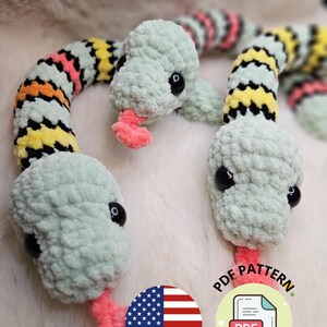 Peut inclure: Serpentin en crochet aux couleurs vert, jaune, rose et orange. La tête du serpent est vert clair avec des yeux noirs et une langue rose. Le corps est rayé de différentes couleurs. Le texte "AnnaleyLoops" et "PDF PATTERN" est également présent.