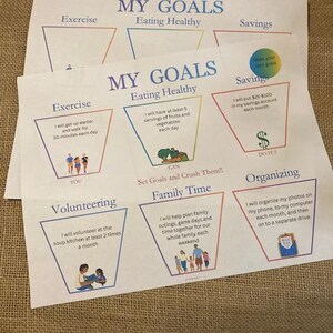 May include: Two sheets of paper with the title "MY GOALS" in blue. The sheets are divided into sections for exercise, eating healthy, and savings, with illustrations and text describing goals. The text includes "Set Goals and Crush Them!!".