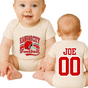 A baby wearing a white onesie with a Kansas City football team logo and the name "Joe" printed on the back.