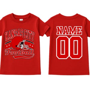 A red t-shirt with the text "KANSAS CITY FOOTBALL" printed on it, along with a football helmet graphic. The t-shirt also has the number "00" printed on the back.
