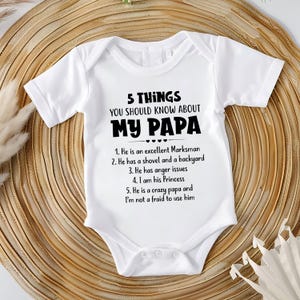 Può includere: Un body bianco a maniche corte per neonati con testo nero: 5 THINGS YOU SHOULD KNOW ABOUT MY PAPA, 1. He is an excellent Marksman, 2. He has a shovel and a backyard, 3. He has anger issues, 4. I am his Princess, 5. He is a crazy papa and I'm not a fraid to use him.