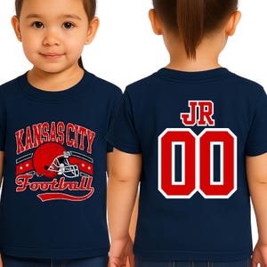 A young girl wearing a navy blue t-shirt with a football helmet and the text "KANSAS CITY FOOTBALL" printed on it.
