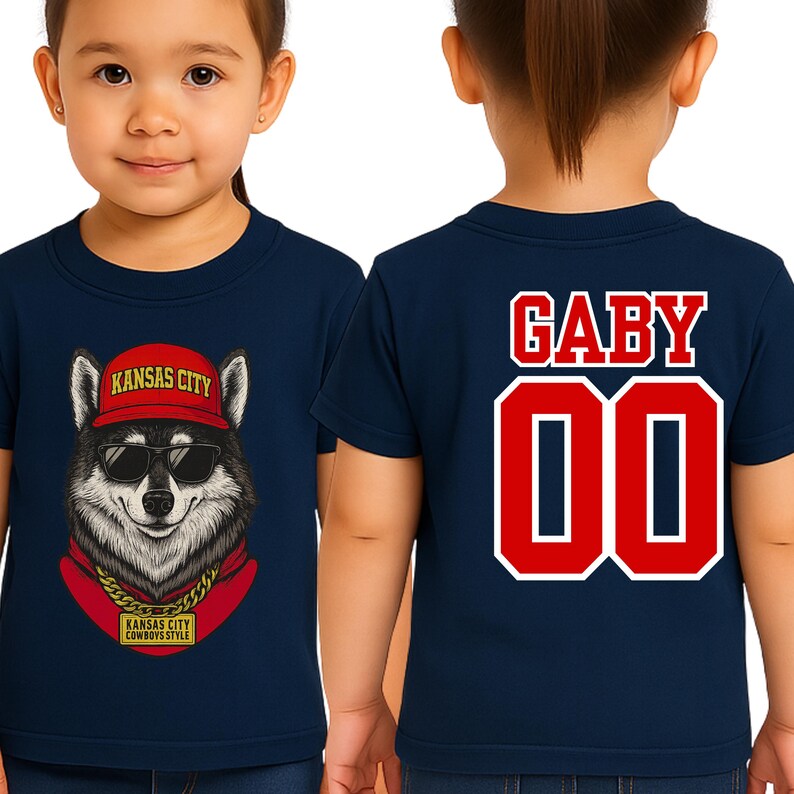 A young girl wearing a navy blue t-shirt with a graphic of a wolf wearing sunglasses and a red hat, along with the text "KANSAS CITY" and "KANSAS CITY COWBOYS".