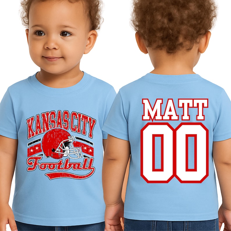 A young child wearing a light blue t-shirt with a graphic of a football helmet and the text "KANSAS CITY FOOTBALL" printed on it. The child's name, "MATT 00", is also displayed on the back of the shirt.