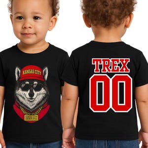 A young child wearing a black t-shirt with a graphic of a wolf wearing sunglasses and a red hat, along with the text "KANSAS CITY" and "COWBOYS STYLE".