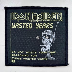 May include: A square black fabric patch featuring the Iron Maiden logo and the text Wasted Years. It includes a graphic of a character with an antenna and the phrase Do not waste your time searching for those wasted years in yellow lettering.