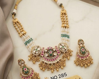 Può includere: Un set in ottone color oro composto da una collana e due orecchini abbinati. La collana presenta fili di perline bianche e verdi, dettagli dorati, smalto rosa e verde e ciondoli pendenti. Il testo recita: NO 285 Brass High gold set.
