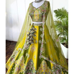 May include: A vibrant yellow and green embroidered lehenga, a traditional Indian garment. The skirt features alternating panels of yellow and green, adorned with floral and geometric patterns. The matching top and sheer dupatta are embellished with intricate embroidery and beadwork.