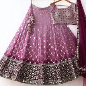 May include: A formal, two-piece outfit in shades of purple and burgundy. The skirt and top are embellished with intricate patterns and sequins. A matching scarf is draped over the shoulder. The outfit is designed for special occasions.