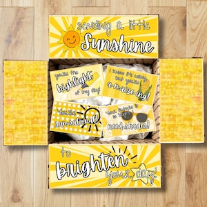 May include: A cardboard gift box with yellow sunburst patterns and text reading sending a little Sunshine to brighten your day. Inside are four cards with yellow graphics and text: you're the highlight of my day, a-maize-ing, sun-sational, and need shades.