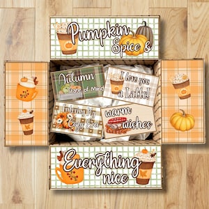 May include: A cardboard gift box filled with white tissue paper, featuring autumn-themed graphics of pumpkins, coffee cups, and plaid patterns. The box flaps display text including Pumpkin Spice, I love you a Latte, and Everything nice.