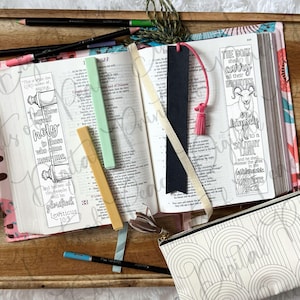 May include: An open book with two illustrated bookmarks featuring text from Leviticus, including a goat drawing and scroll imagery. The book is surrounded by colored pencils, a black bookmark with a pink tassel, and a white pencil case with an arch pattern.