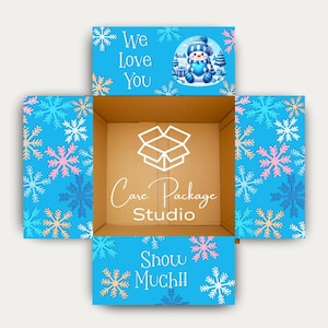 May include: An open cardboard box with blue flaps decorated with snowflakes. The top flap reads "We Love You" with a snowman illustration. The bottom flap says "Snow Much!!" The inside of the box has the text "Care Package Studio".
