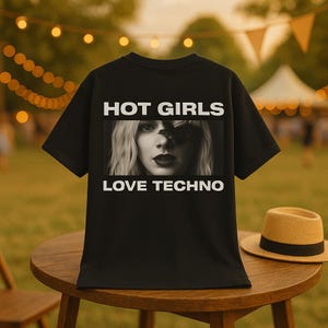 Puede incluir: Camiseta negra con el texto "HOT GIRLS LOVE TECHNO" encima y debajo de una imagen en blanco y negro del rostro de una mujer. Un sombrero de paja descansa sobre una mesa de madera junto a la camiseta. El fondo está borroso con elementos exteriores.
