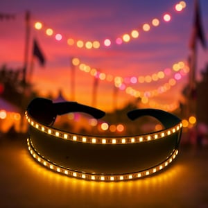 Può includere: Occhiali da sole senza montatura con montatura nera e una striscia luminosa a LED gialla brillante. Lo sfondo presenta un tramonto e luci a catena, creando un'atmosfera vibrante e festosa.