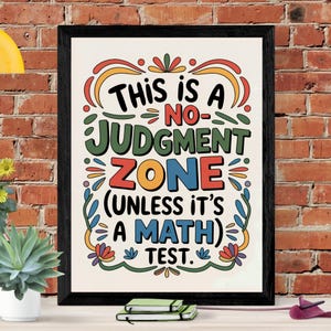 以下が含まれることがあります： 「THIS IS A NO-JUDGMENT ZONE (UNLESS IT'S A MATH) TEST」と書かれた額入りのアートプリント。テキストは様々な色とフォントで、装飾的な花の要素で囲まれています。フレームは黒です。