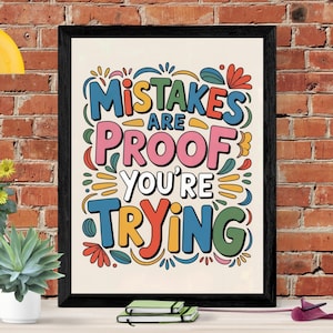 May include: A framed art print with the words "Mistakes are Proof You're Trying" in colorful, stylized lettering. The artwork features a black frame and is set against a cream-colored background. Decorative floral and leaf elements surround the text.
