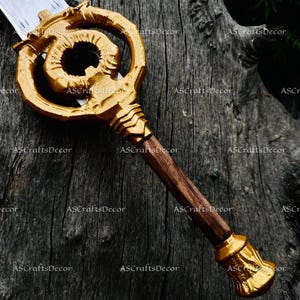 May include: A decorative sword with a gold-coloured key-shaped hilt and a wooden handle. The blade is silver. The hilt features an ornate design with a spiral element. The handle is a dark brown colour, and the pommel is gold.