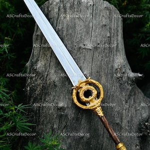 May include: A decorative sword with a silver blade and a gold-coloured handle. The handle features an intricate design and a dark brown grip. The sword is displayed against a textured wooden background.