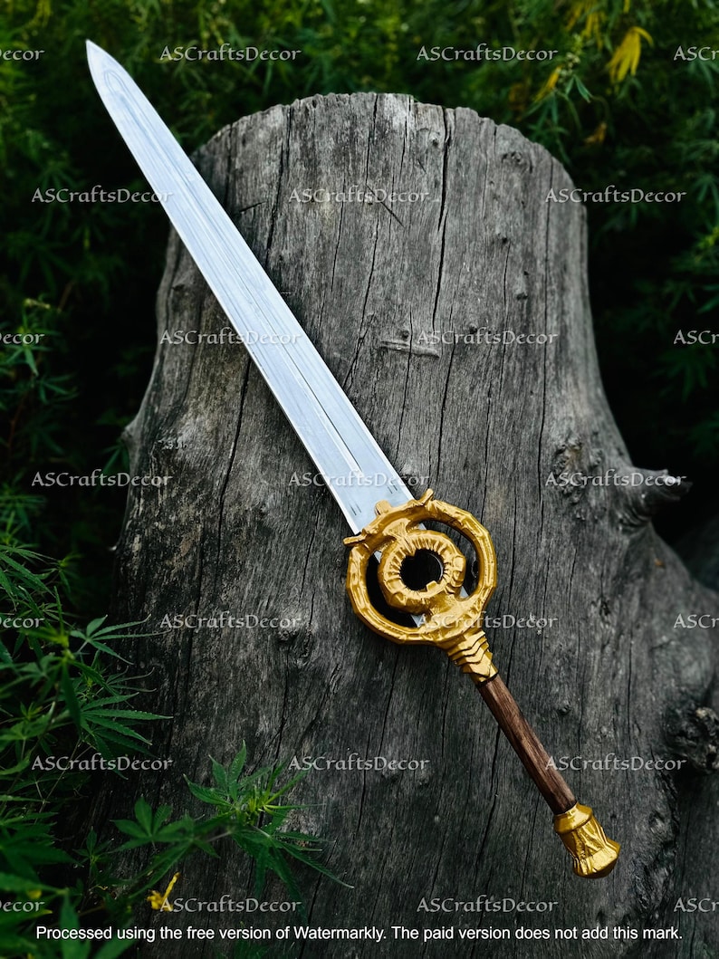 May include: A decorative sword with a silver blade and a gold-coloured handle. The handle features an intricate design and a dark brown grip. The sword is displayed against a textured wooden background.