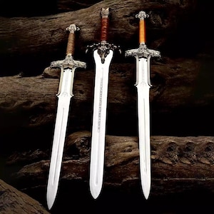 May include: Three ornate swords with silver blades and detailed hilts are displayed against a dark, textured background. The handles are wrapped in brown leather or cord, and the crossguards feature intricate designs. The swords vary slightly in handle and hilt design.