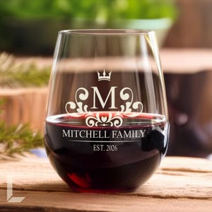 Op de afbeelding: Een helder, steelloos wijnglas gevuld met rode wijn. Het glas heeft een wit ge&euml;tst ontwerp met een kroonpictogram boven de letter M, omringd door krulwerk. Daaronder staat de tekst MITCHELL FAMILY en EST. 2026 in het wit.
