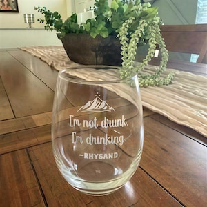 Op de afbeelding: Een helder wijnglas zonder steel met een witte gegraveerde bergafbeelding boven de tekst "I'm not drunk. I'm drinking. -RHYSAND". Het glas heeft een ronde komvorm en is gemaakt van transparant glasmateriaal met een gladde afwerking.