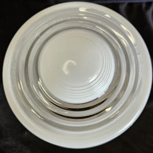 May include: A circular glass plate featuring a raised, smooth central dome surrounded by concentric, recessed rings. The design is entirely clear and transparent, showcasing a clean, reflective surface with a uniform, polished finish throughout.