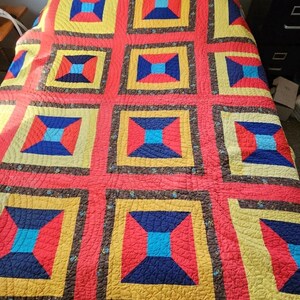 May include: A colorful quilt with a repeating geometric pattern. The quilt features large squares in red, yellow, blue, and brown. The squares are arranged in a grid-like fashion, creating a visually appealing design. The quilt is likely made of cotton or a similar fabric.