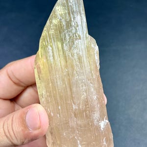 Könnte beinhalten: Ein durchscheinendes, blassgelbes Spodumen-Kristallexemplar mit einer ausgeprägten länglichen, prismatischen Form und vertikalen Streifen entlang seiner Länge. Das Mineral weist eine natürliche, rohe Textur mit glasigem Glanz und variierender Farbintensität auf.