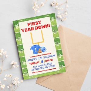 May include: A football-themed birthday invitation with the text "FIRST YEAR DOWN!" in red. The invitation includes a blue jersey, helmet, and football graphic. The details include the birthday date, time, and location. A brown envelope is next to the invitation.
