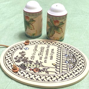 May include: A decorative ceramic garden sign with the text "Life is a Garden and Friends are the sunshine that make it grow." Two salt and pepper shakers with a fruit and leaf design are also in the image.