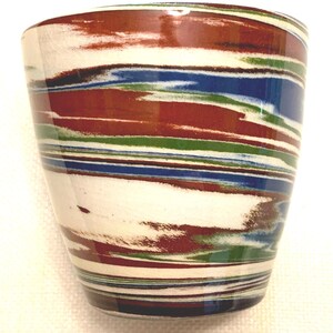 May include: A ceramic cup featuring a marbled pattern with horizontal bands of white, deep red, forest green, and royal blue. The surface has a smooth, glossy finish with a slightly tapered cylindrical shape and a wide, open top rim.