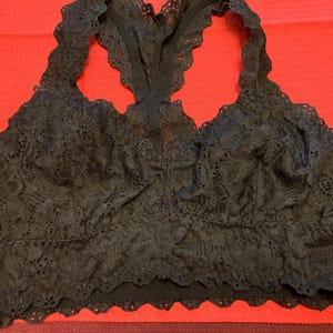 May include: Black lace bralette with a racerback design. The bralette features a scalloped trim along the bottom and around the straps. The intricate lace pattern covers the entire bralette.