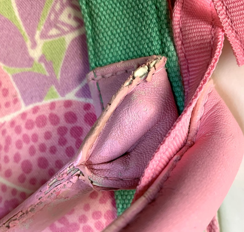 May include: Close-up of a pink handbag with a floral pattern. The bag features a pink leather strap and a green fabric strap. The floral pattern includes pink and white shapes. The bag's leather shows signs of wear.