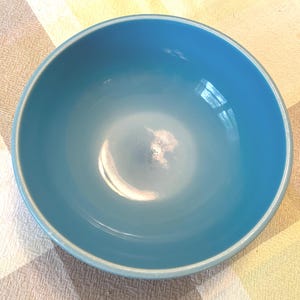 May include: A round, smooth, solid blue bowl with a glossy finish. The interior of the bowl is a consistent, vibrant shade of blue, featuring a wide, open circular rim and a deep, curved basin that reflects light on its polished surface.