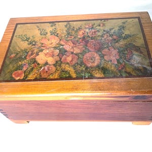 May include: A rectangular wooden box with a hinged lid featuring a printed floral design. The box has a natural wood grain finish on the sides and top, with visible finger joints at the corners and a flat base. The floral print displays orange and red flowers.