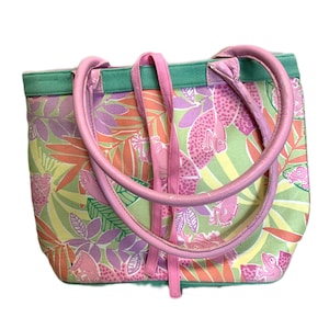 May include: A colorful tote bag with a tropical pattern featuring pink frogs, fish, and leaves. The bag has pink handles and straps, with a green trim. The bag is made of a durable fabric.